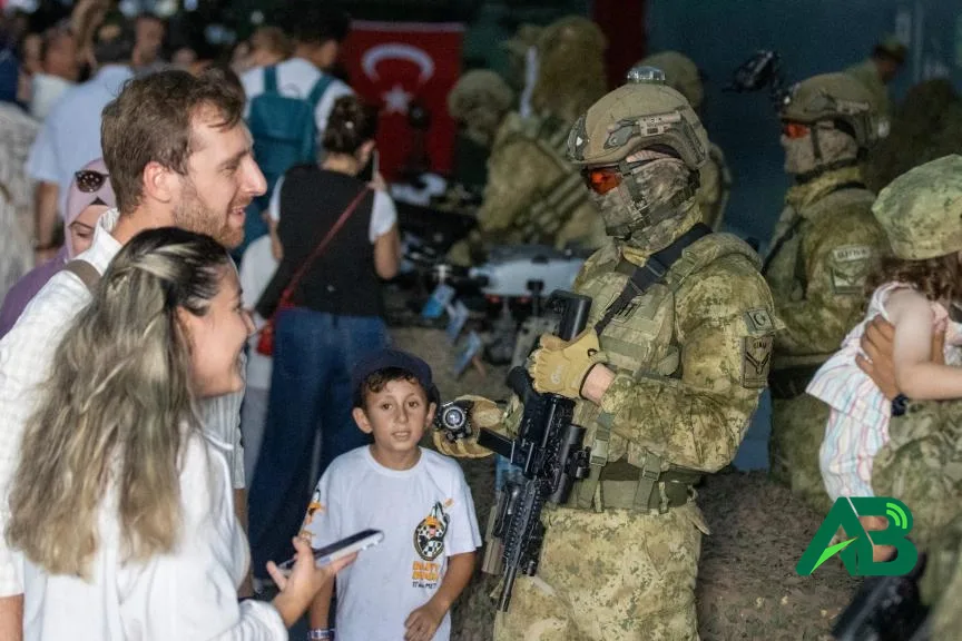 TEKNOFEST alanında askeri kamuflajlı bir askerle sohbet eden ziyaretçiler ve çocuklar.