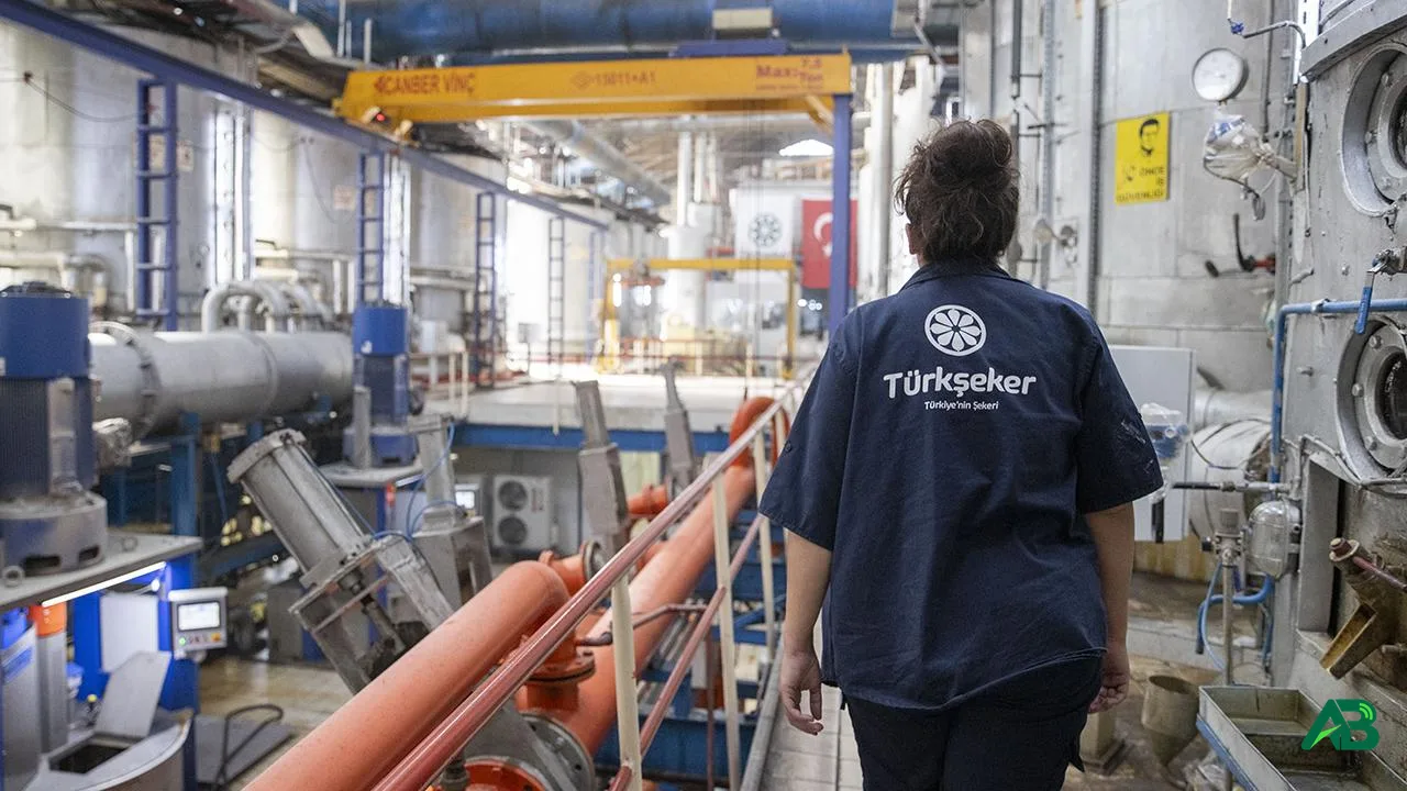 Türkşeker logolu üniforma giymiş bir çalışanın endüstriyel şeker fabrikası içerisinde yürüdüğü an.